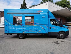 Blauer Truck mit Bedienungsfenstern auf der Seite, geparkt auf einem Platz