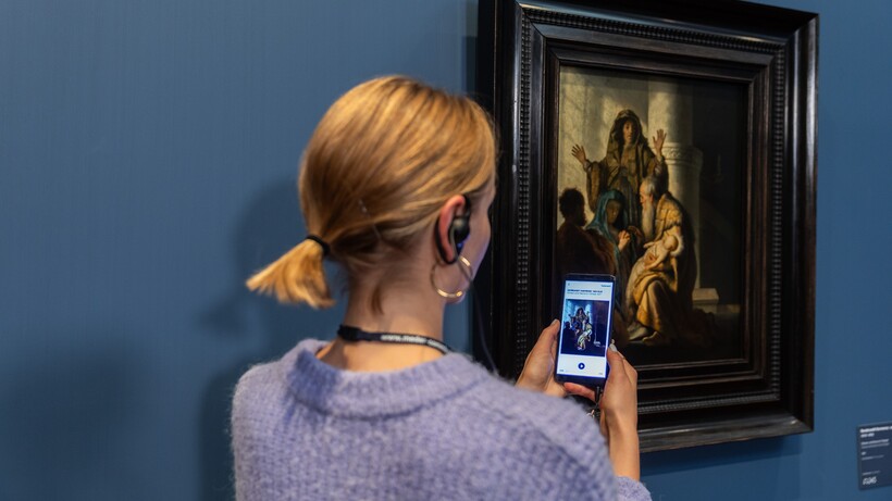 Eine Frau mit Handy und Kopfhörern vor dem Gemälde von Rembrandt Harmensz. van Rijn (1606–1669)