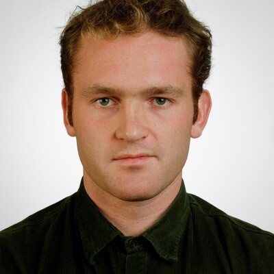 Portraitfoto eines jungen Mannes mit braunem Haar in schwarzem Poloshirt vor weißem Hintergrund